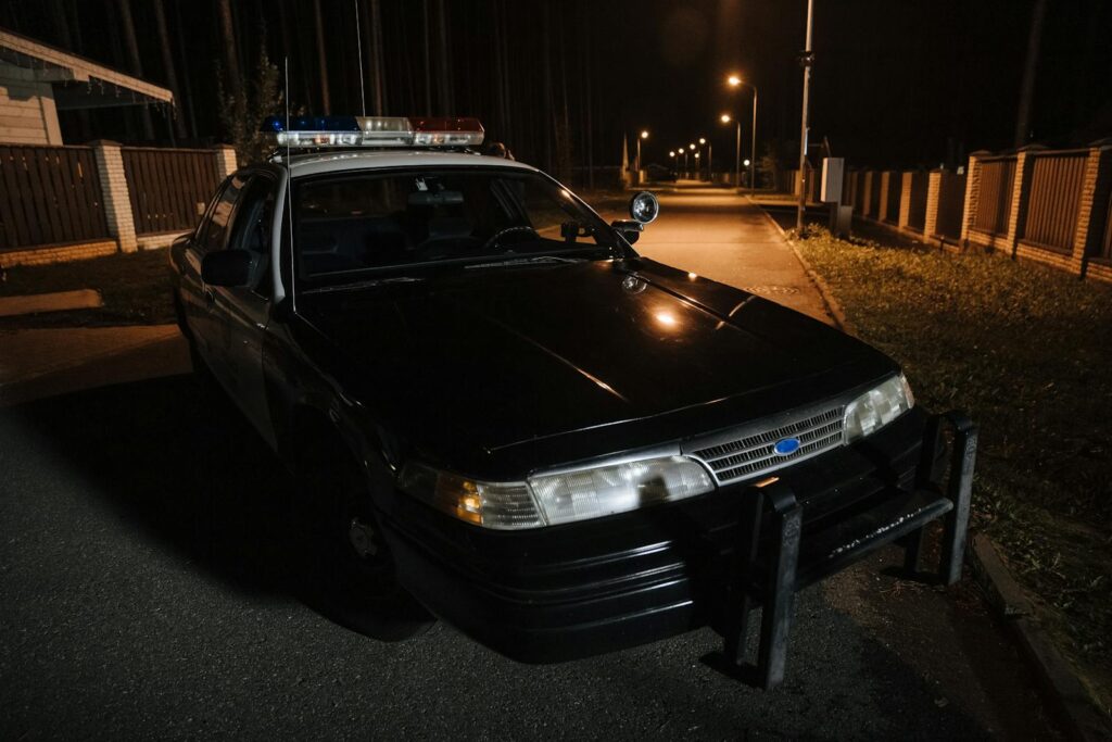 A police car parked on a quiet street at night with streetlights illuminating the road.