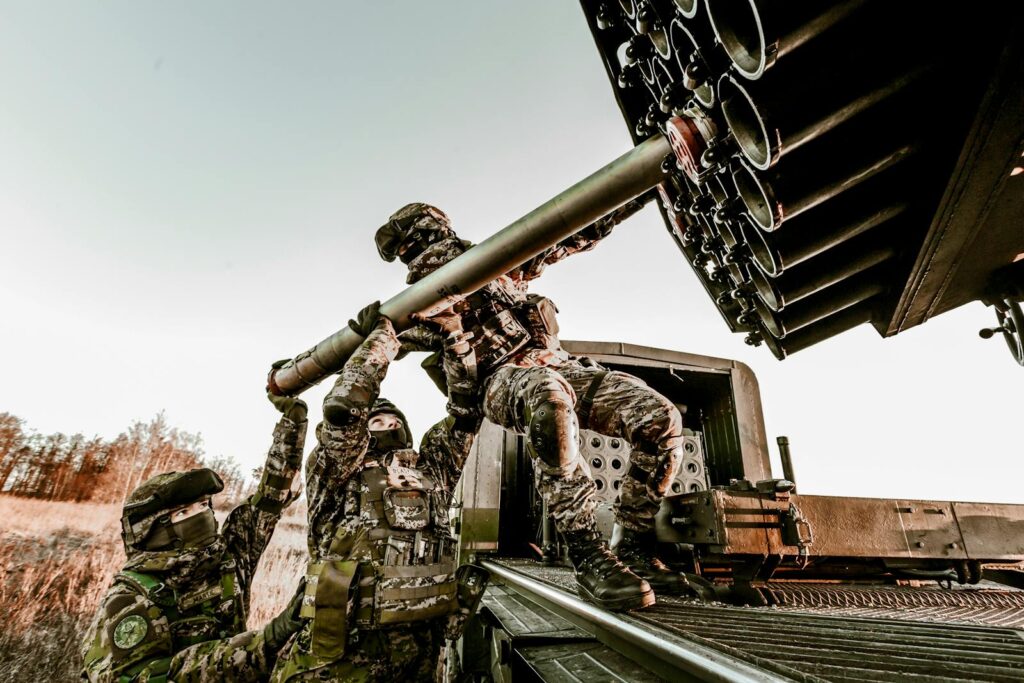 Soldiers in camouflage uniforms loading artillery equipment during a military field operation.