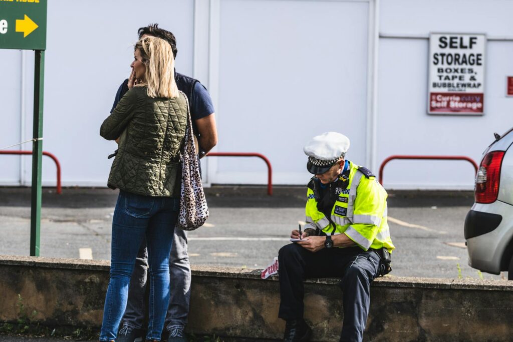 Police officer writing a ticket near a self-storage area with people in the background.