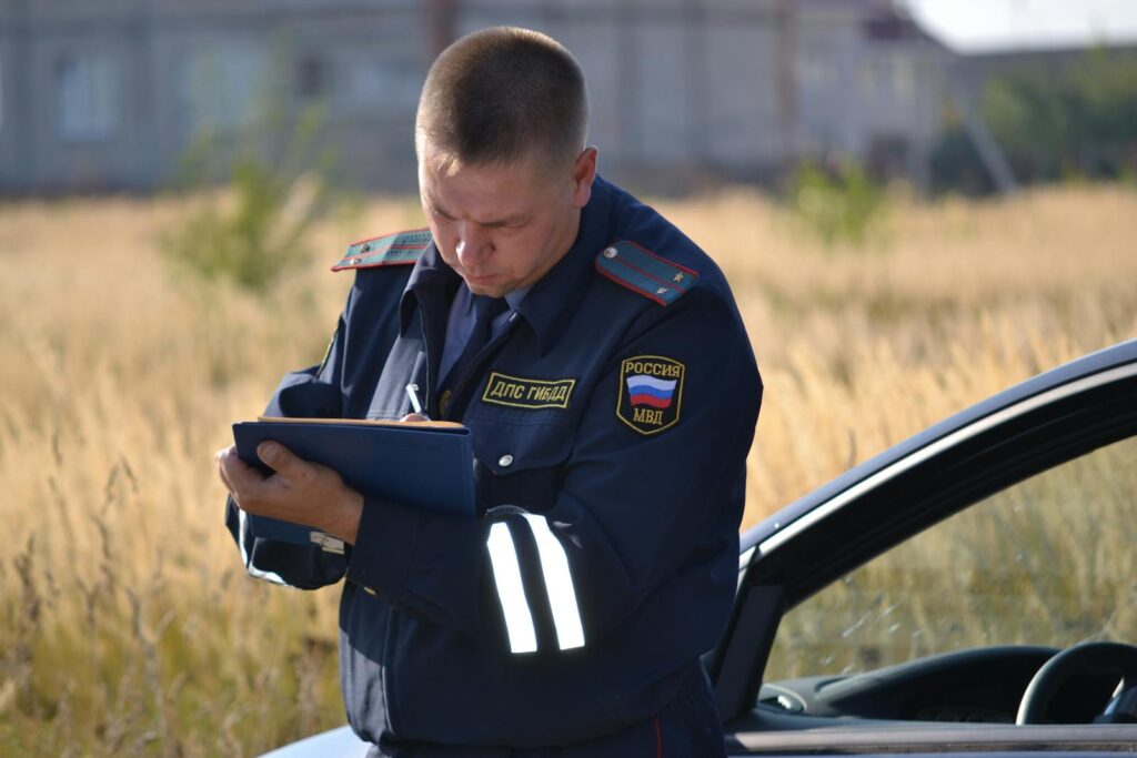 Police officer in uniform taking notes beside a car in a field.