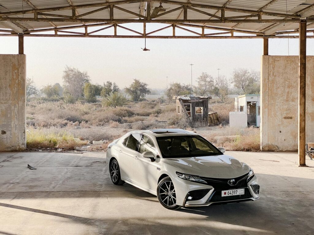 A sleek white sedan parked inside an open, abandoned garage in a rustic, grassy environment.