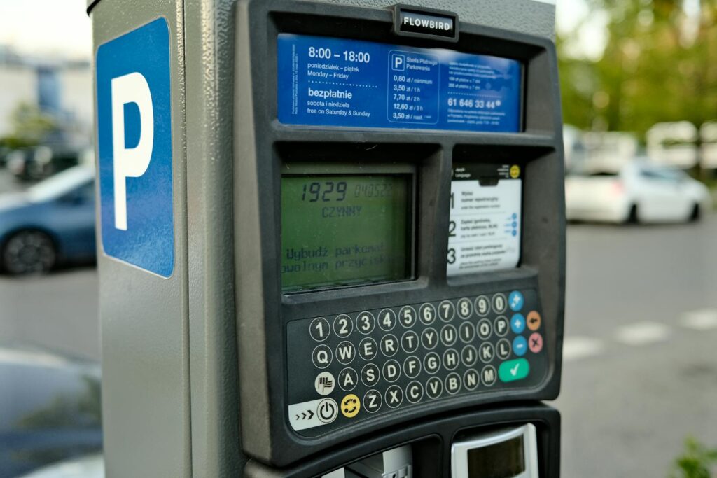 Close-up of a digital parking meter in a city setting with cars in the background.