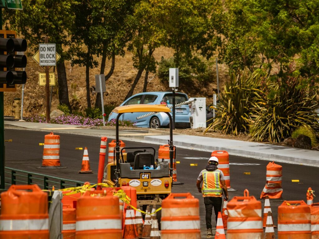 A road construction worker surrounded by safety cones on a street in daylight.