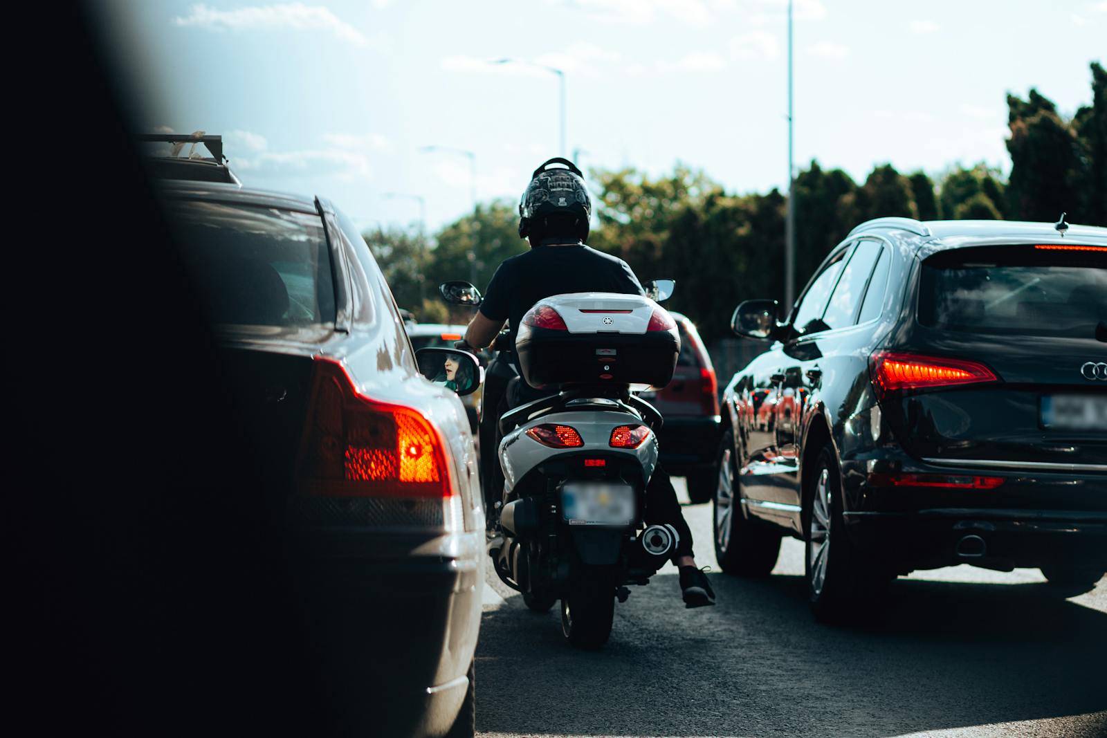 Motorcyclist maneuvering through city traffic jam on sunny day.