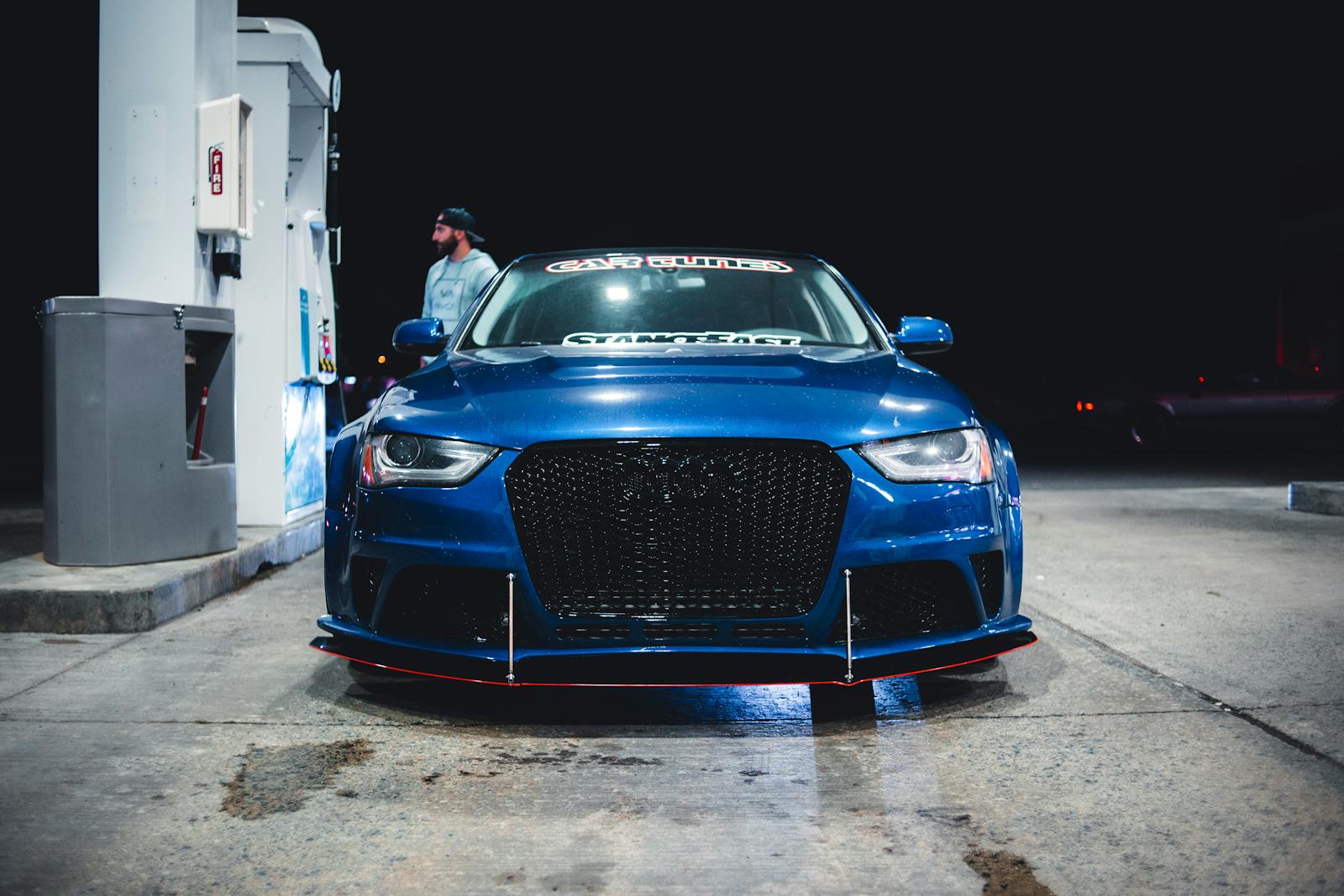A striking blue car parked at a gasoline station at night, emphasizing modern vehicle design.