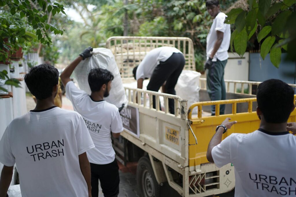 Men managing urban waste, loading trash into truck in Kochi, India.
