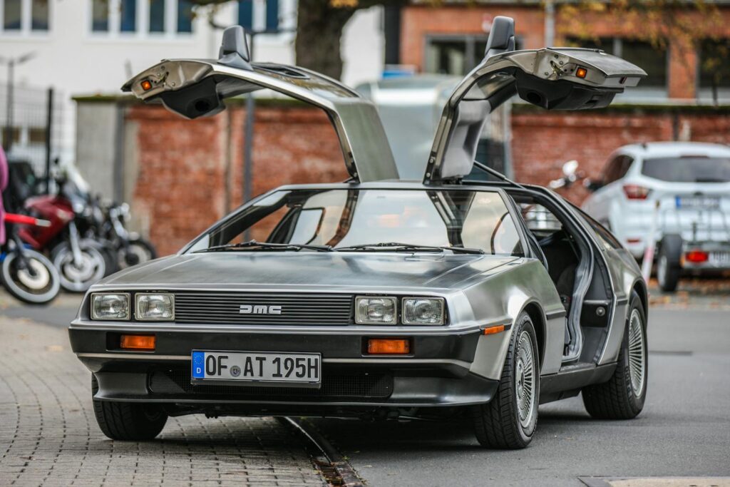 DeLorean DMC-12 with distinctive gullwing doors open, parked outdoors.