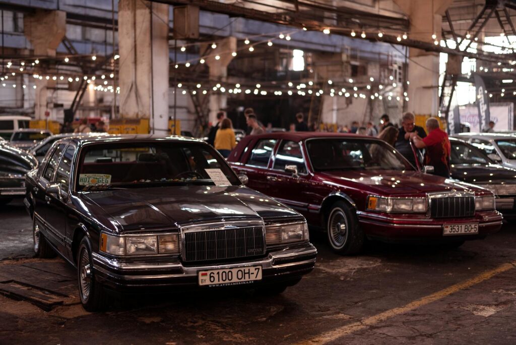 Classic luxury cars displayed in an indoor auto show setting with a vintage ambiance.