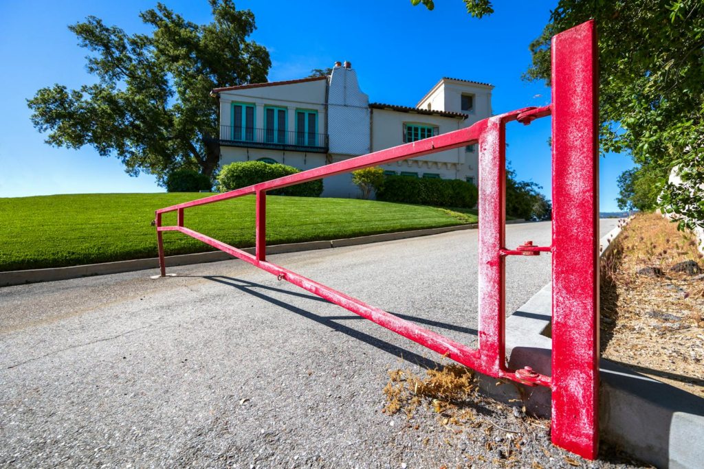 A bold red gate on a sunny day, marking the entrance to a beautiful hillside residence.