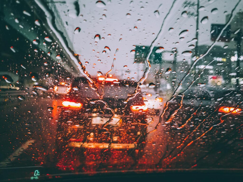 Blurred city traffic seen through a rain-soaked windshield, capturing the moody atmosphere of a wet day.