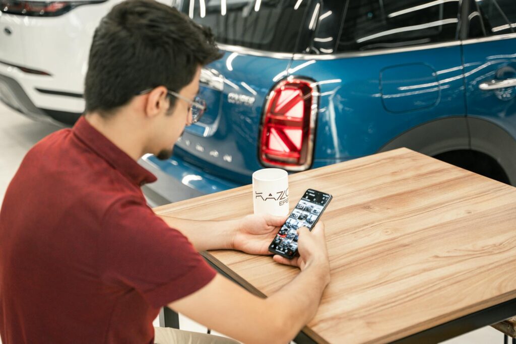 Young man at car dealership using smartphone. Modern cars in background.