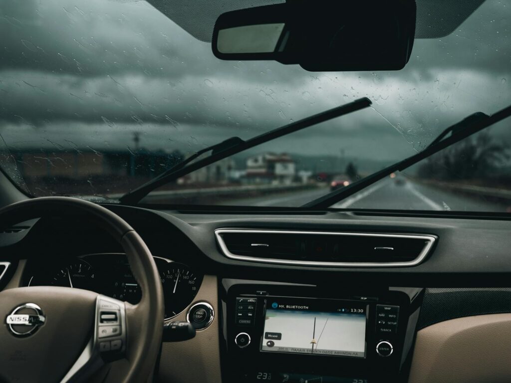 Interior view of a car on a rainy road, capturing steering wheel and dashboard.