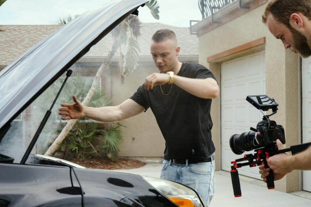 A man films car trouble with smoke using a handheld camera outdoors.