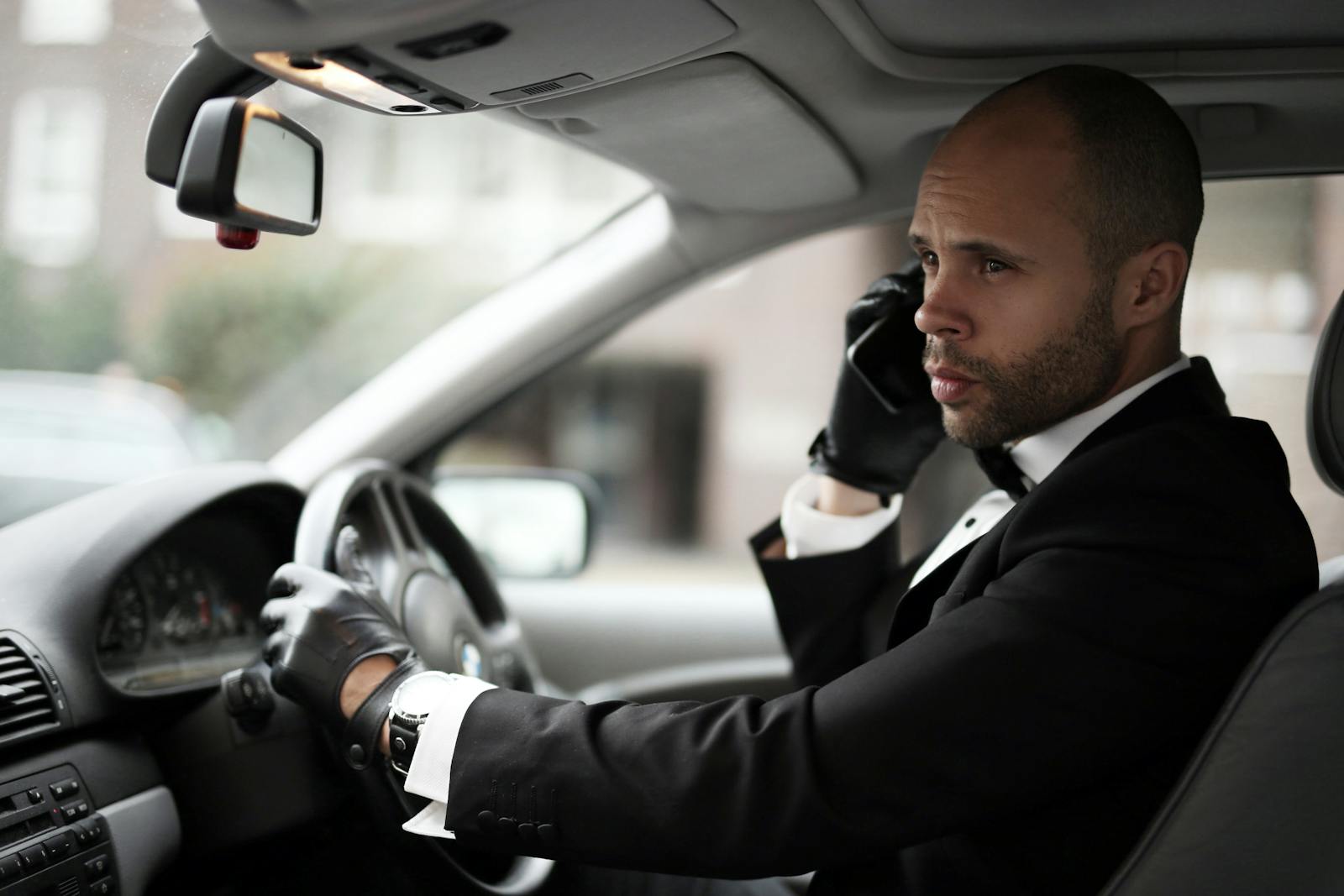 Sophisticated man in suit driving a luxury car while on a phone call, conveying elegance.