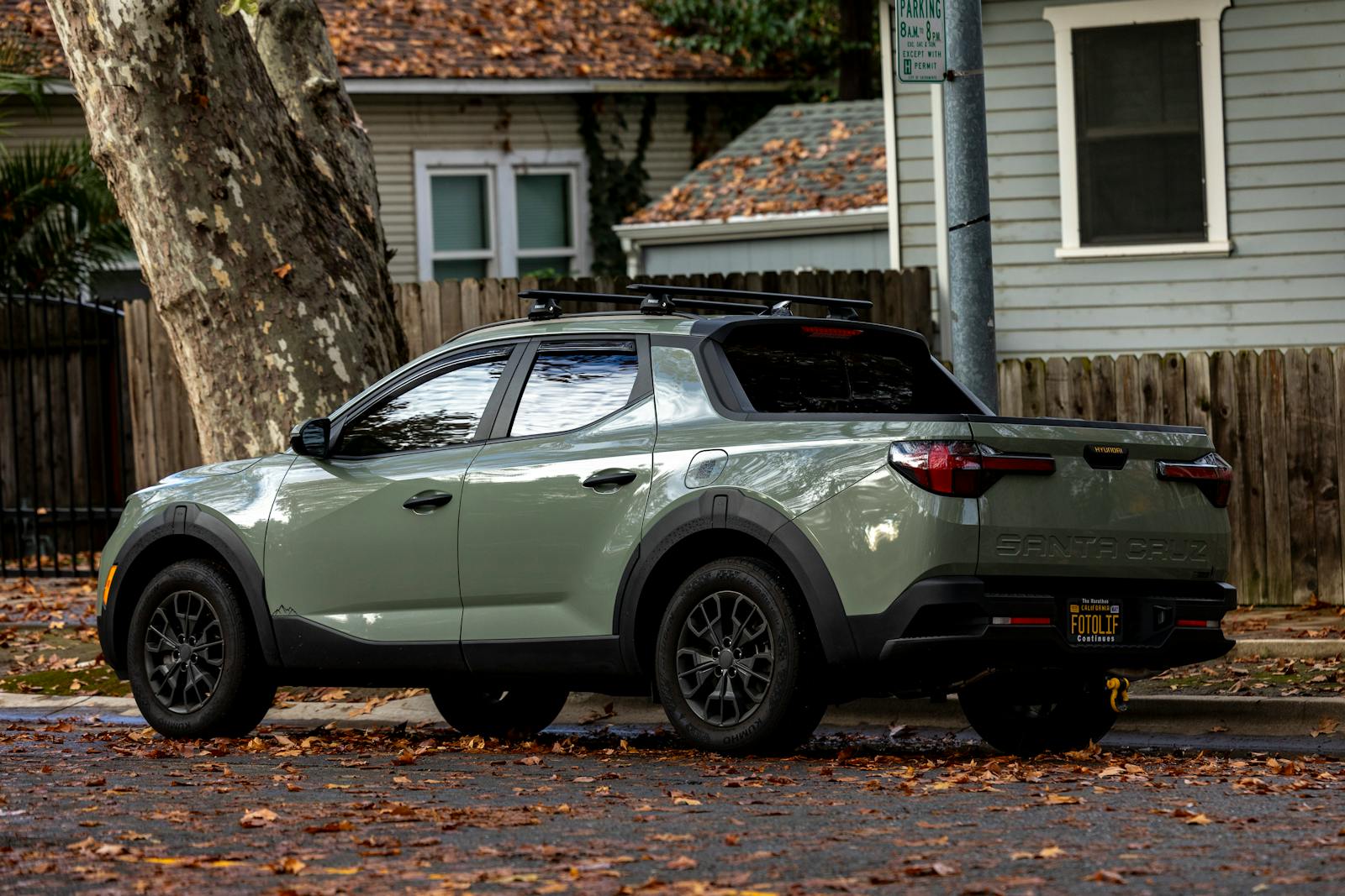 Gray pickup truck parked on a leaf-covered suburban street in autumn.