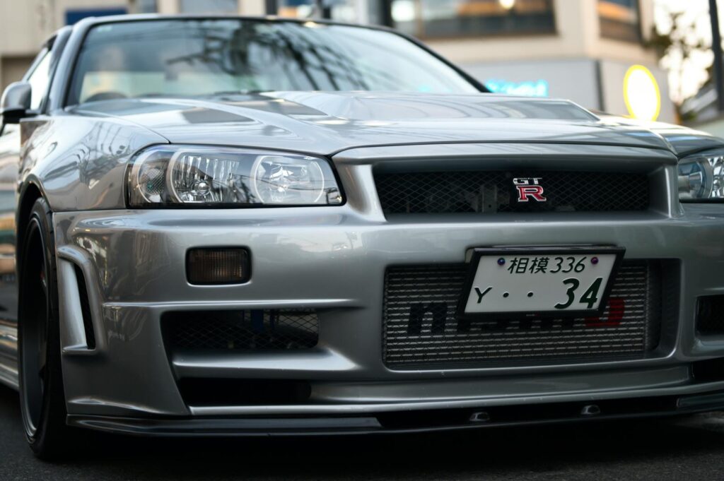 Close-up of a silver Nissan Skyline R34 GTR parked on a Tokyo street, showcasing iconic design.