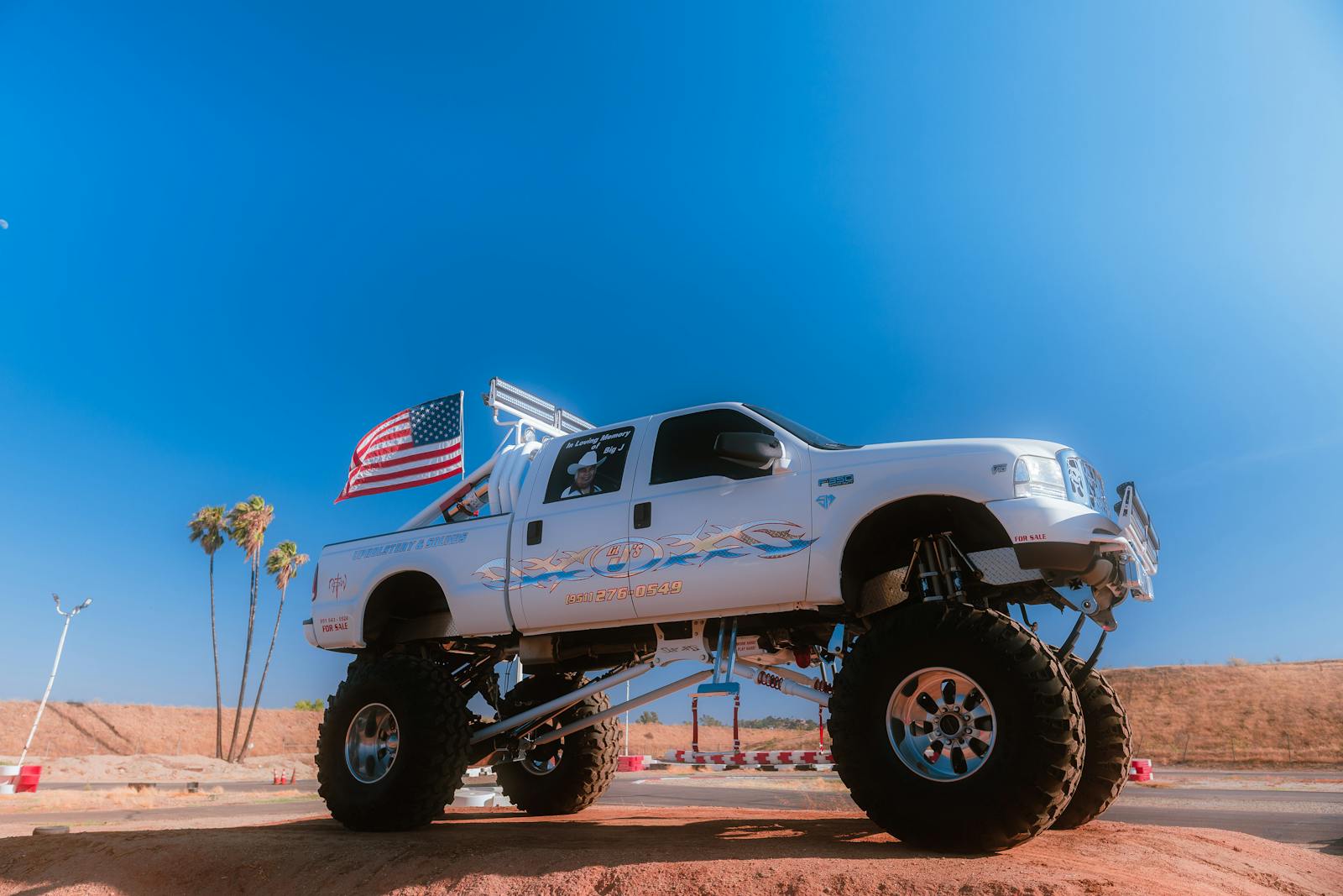 Lifted truck with American flag waving in the desert under clear blue skies.