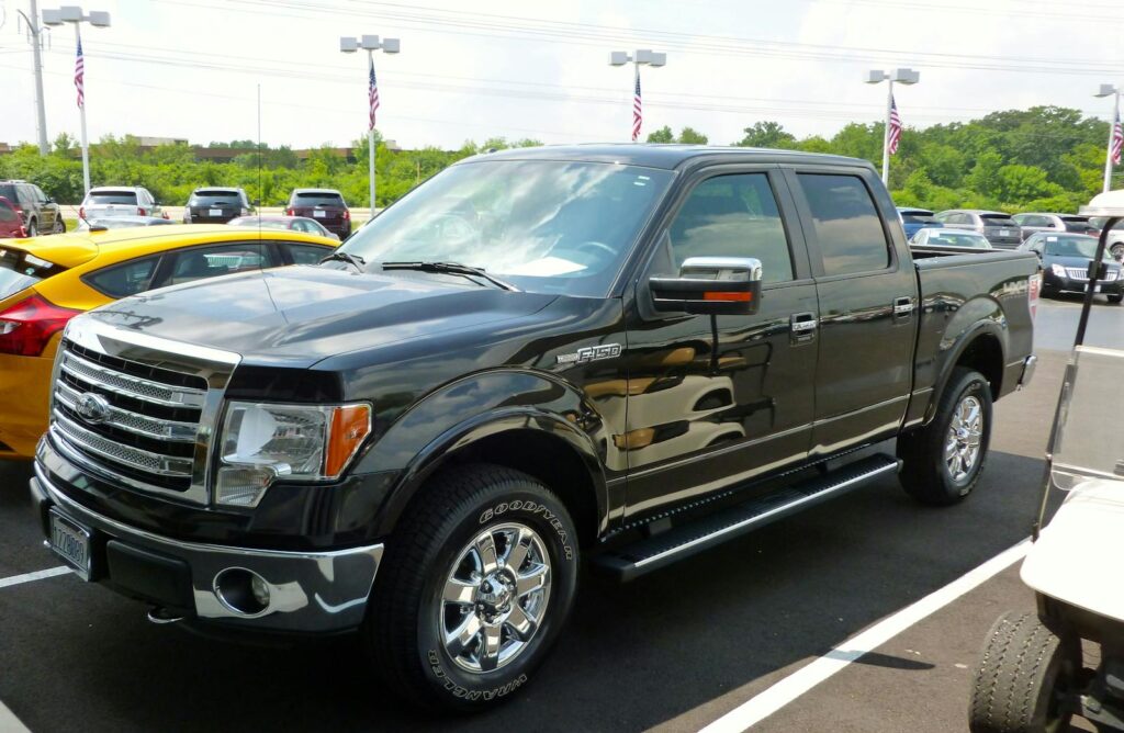 Black Ford F-150 pickup truck displayed at an outdoor dealership lot on a sunny day.