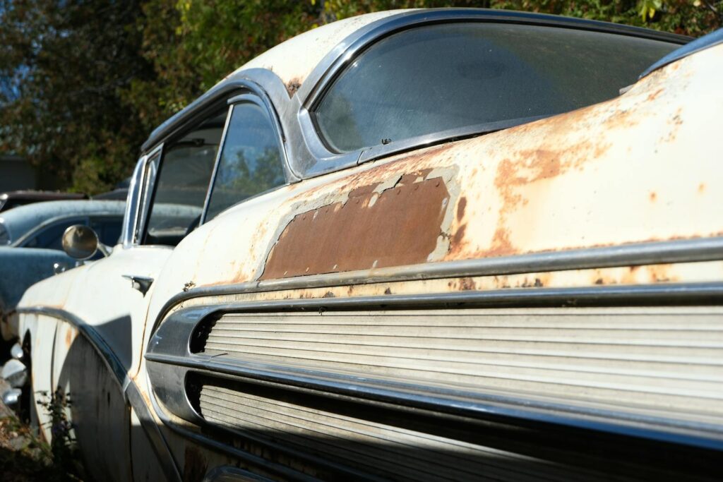 Close-up of a rusted classic car in an outdoor junkyard setting, showcasing vintage design.
