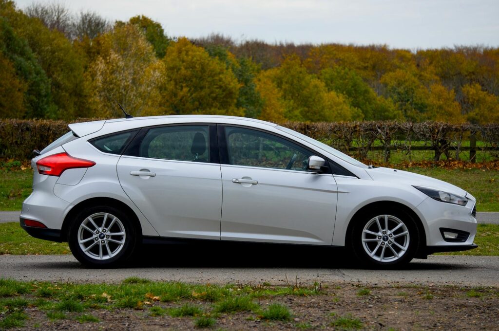 A silver Ford Focus hatchback parked outdoors with autumn foliage in the background in England.
