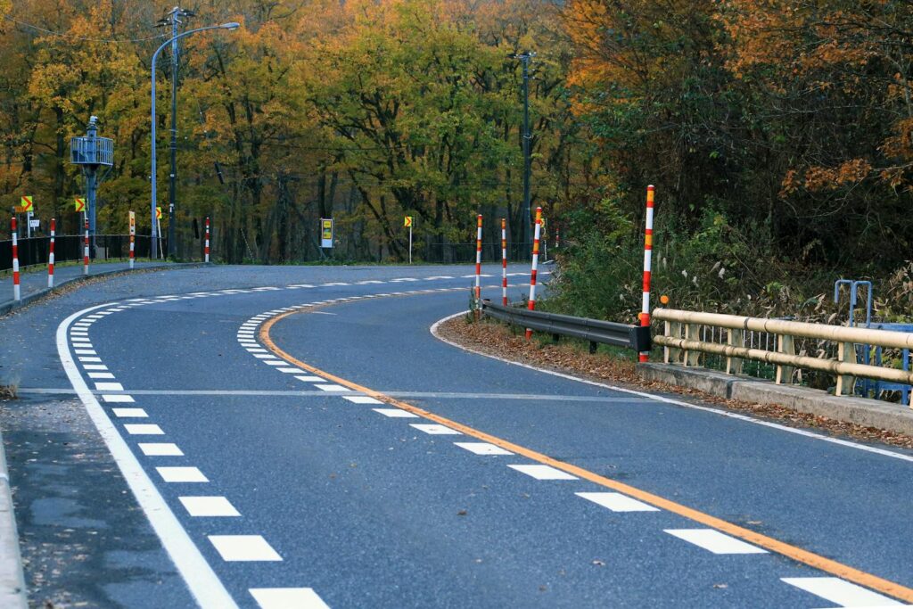 Curved road winding through vibrant autumn forest, showcasing fall foliage and road markings.