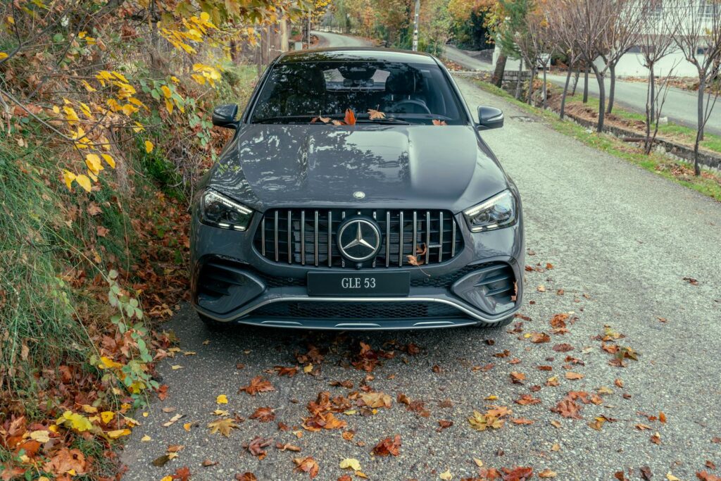 Front view of a Mercedes-Benz GLE 53 surrounded by colorful autumn foliage on a scenic road.