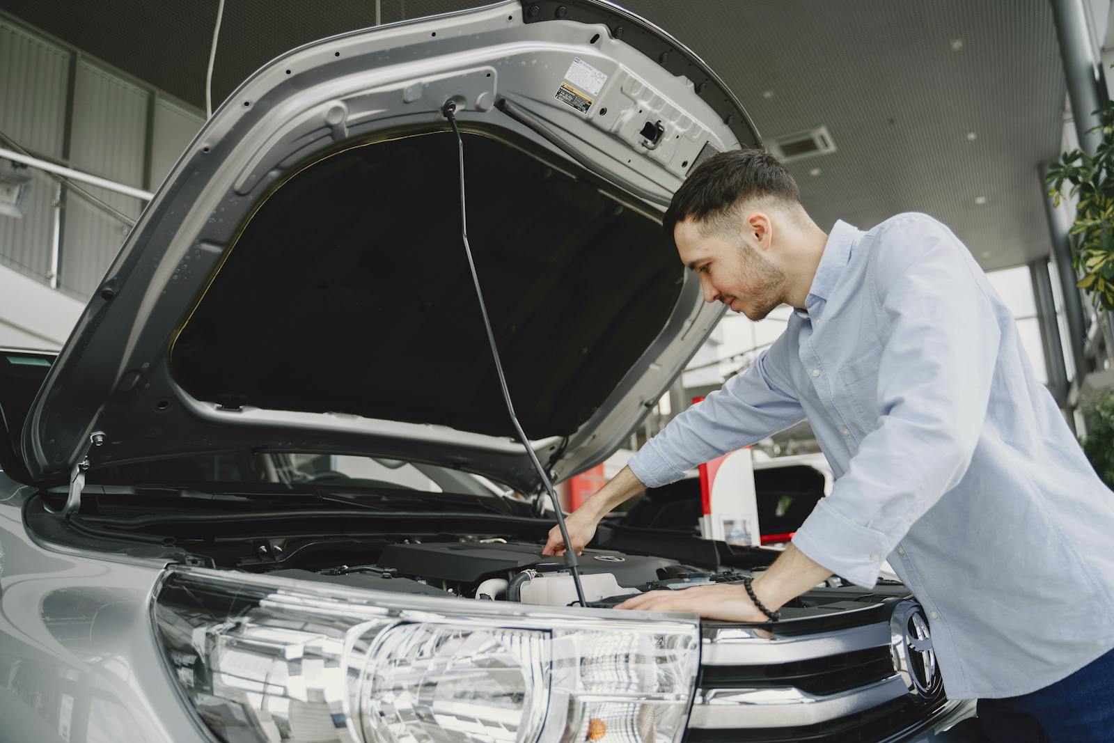 A man in a blue shirt examines a car's engine in a modern vehicle showroom.