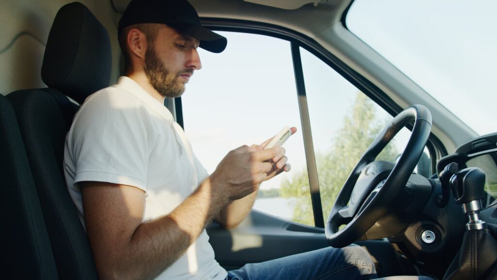 Side view of a man using a smartphone in a parked vehicle on a sunny day.