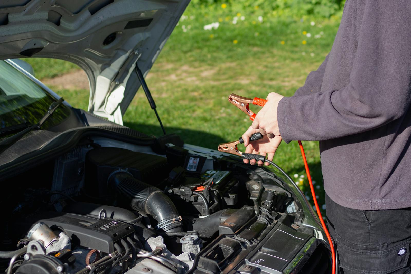 Man using jumper cables on car engine outdoors on a sunny day. Vehicle maintenance and repair concept.