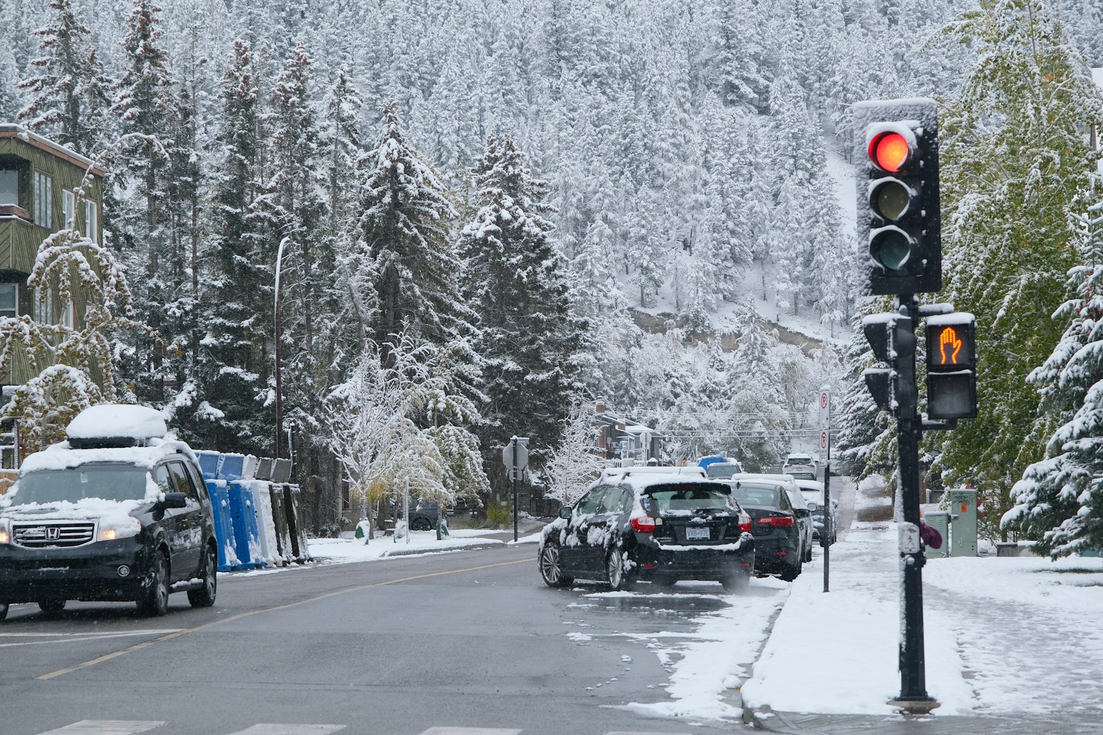 Traffic light on a snowy street with cars.