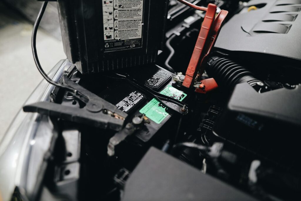 Detailed view of a car battery being jump-started with cables in an engine bay.