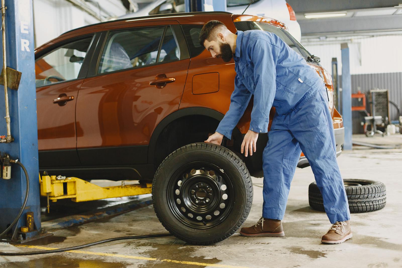 Mechanic in blue coveralls replacing tire on red SUV in repair shop garage.