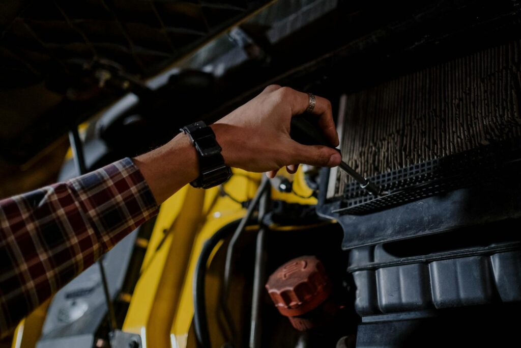 Close-up of a mechanic's hand using a screwdriver to inspect a vehicle's engine.