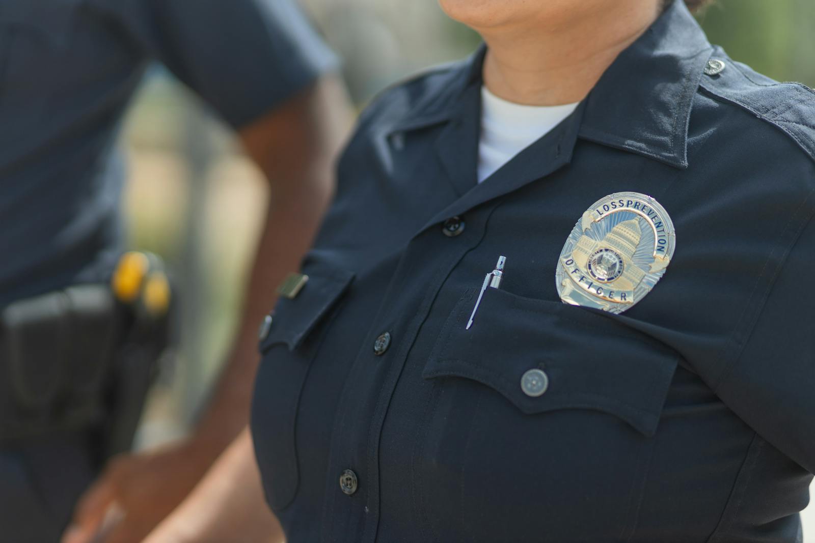 Close-up of police officers in uniform, displaying badge and radio outdoors.