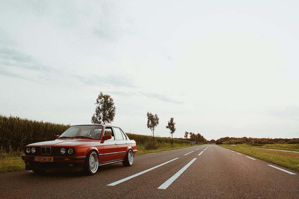 A classic red BMW sedan parked on a scenic countryside road during daylight.