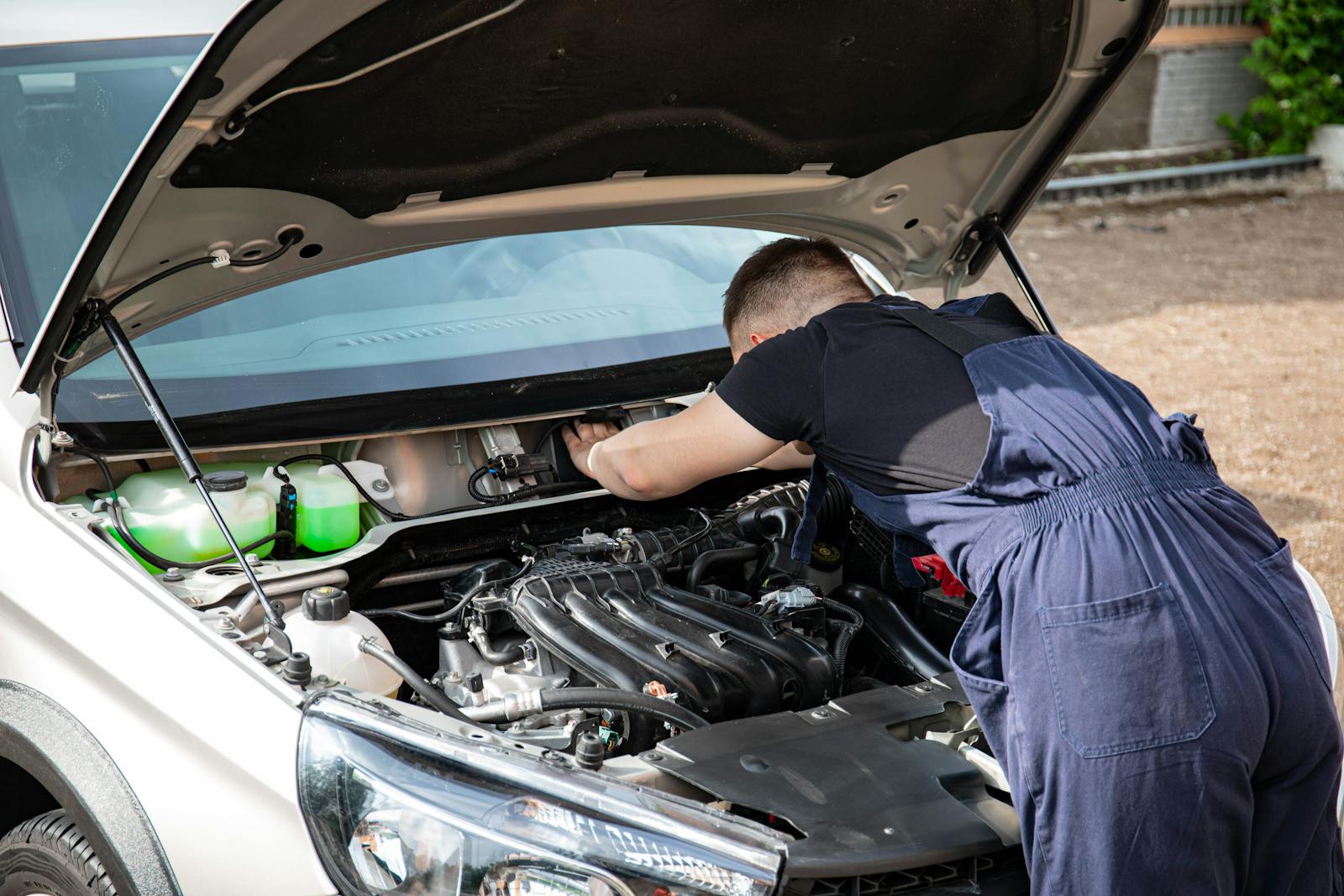 A skilled mechanic works on a car engine in an outdoor setting, showcasing automotive maintenance.