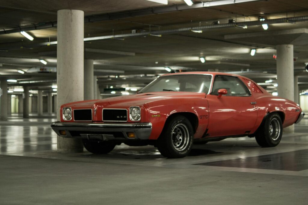 Classic red Pontiac GTO parked in an urban parking structure showcasing vintage muscle car design.