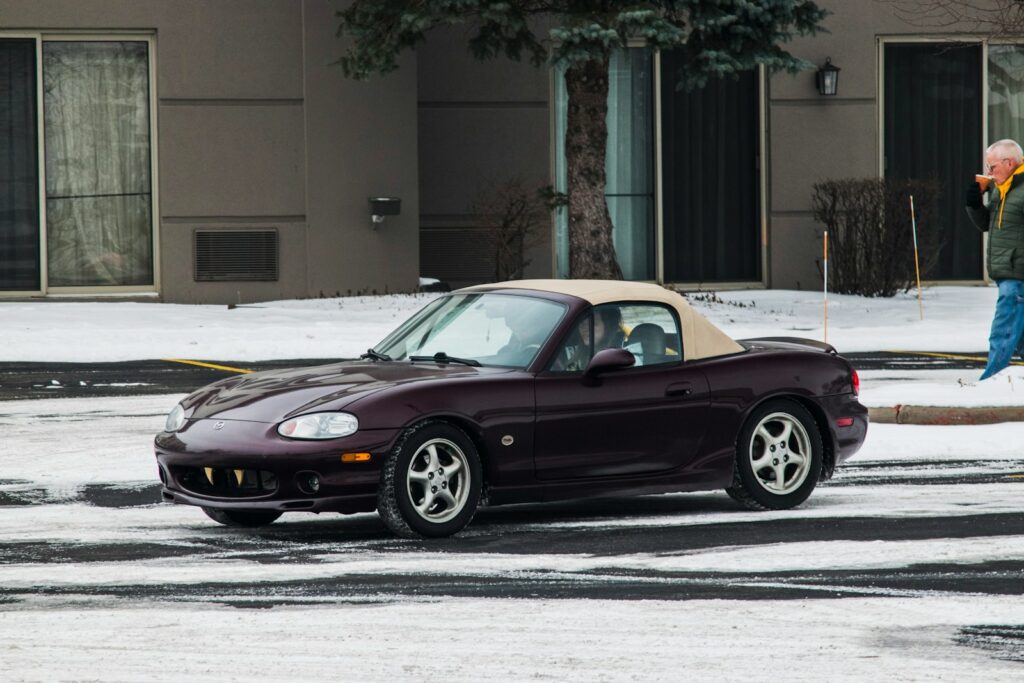 A burgundy convertible sits in a snowy parking lot.