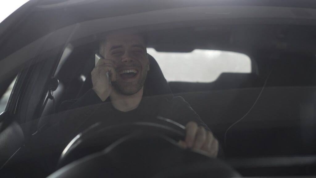 Man laughing while talking on phone in car