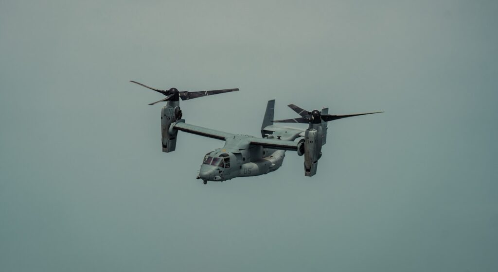 A gray osprey aircraft flies in a cloudy sky.