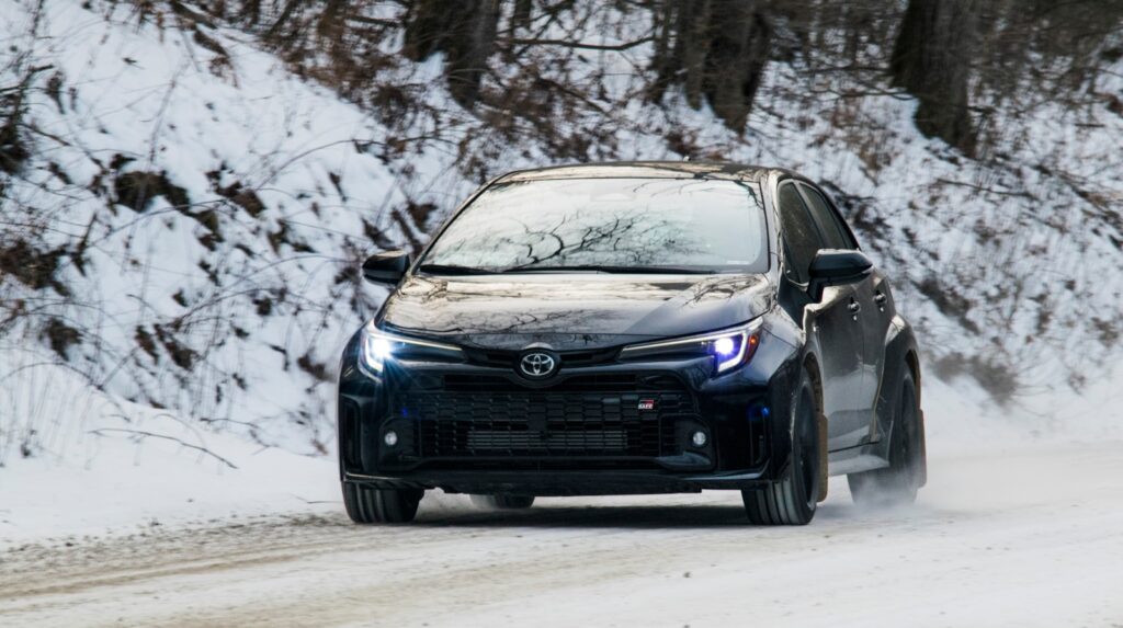 A black car drives through snowy conditions.