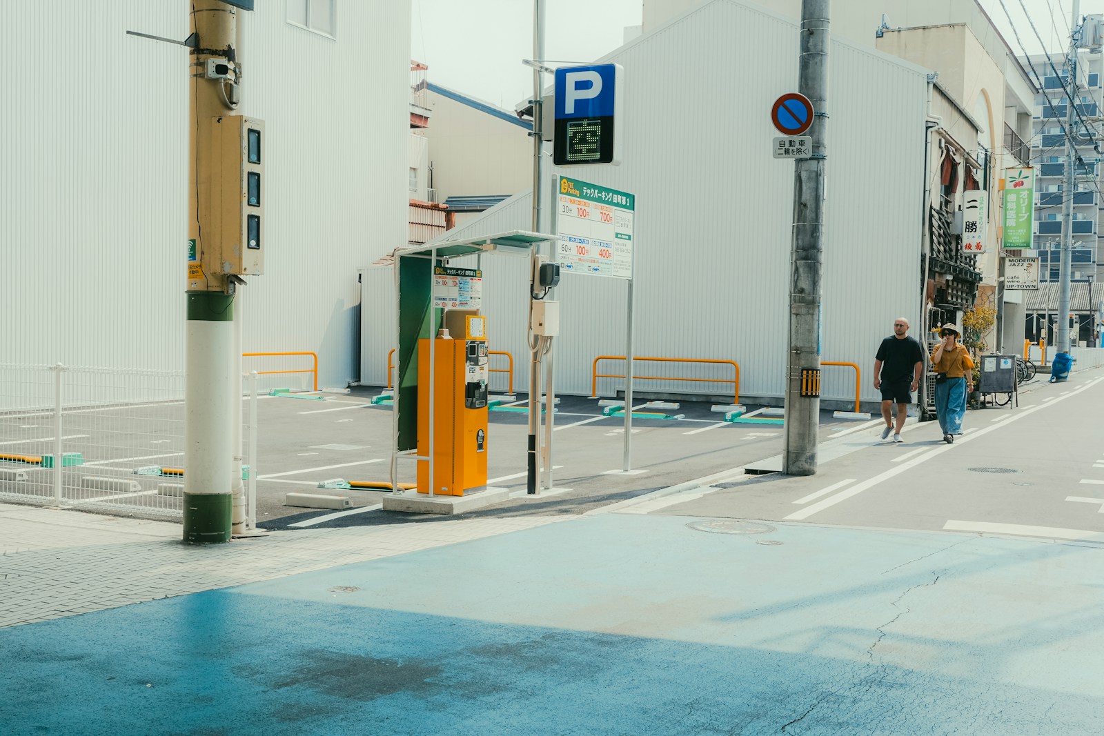 Two people walk down a street with buildings.