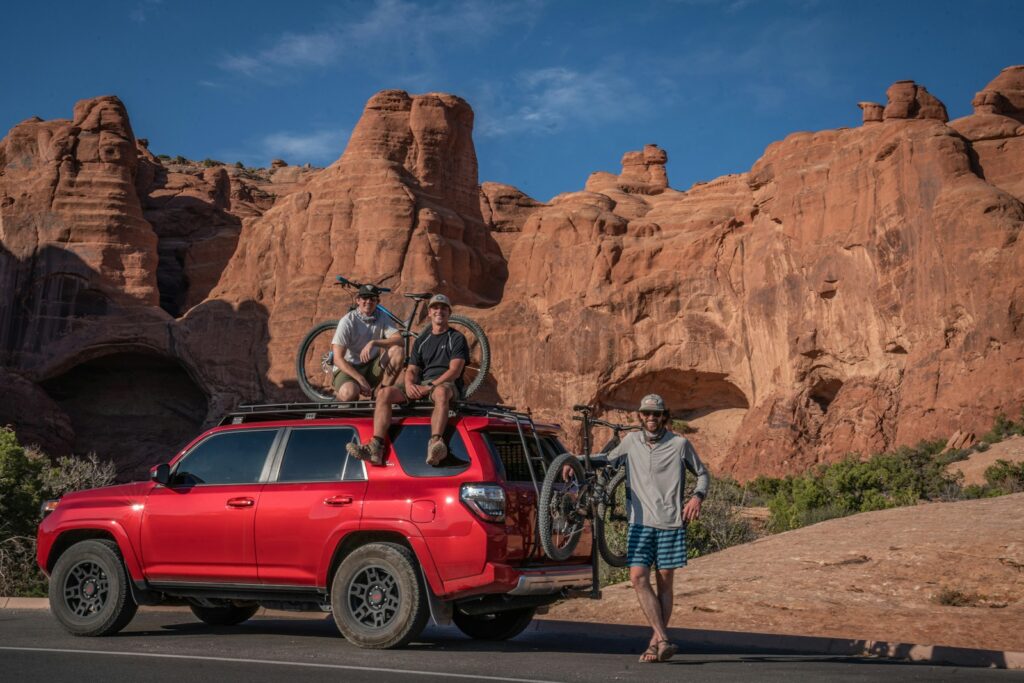 man in white t-shirt and blue denim jeans standing beside red car during daytime