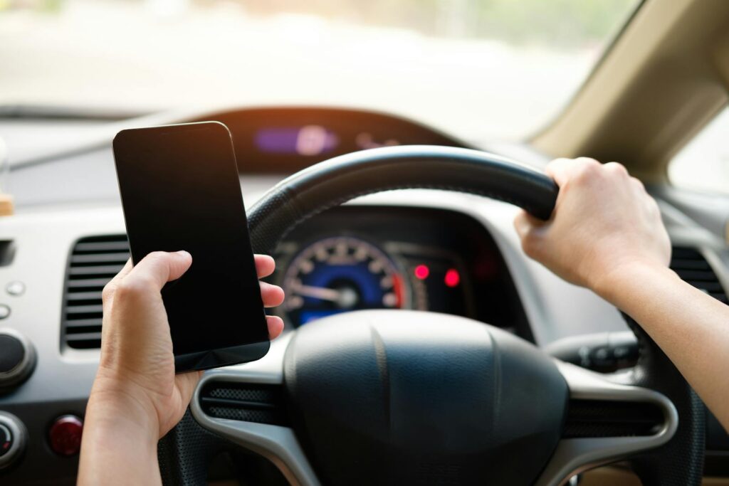A driver uses a smartphone while steering a vehicle, showcasing distracted driving risks.