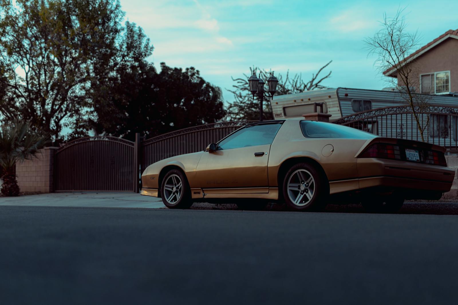 A vintage yellow coupe parked on a quiet residential street with a soft evening glow.