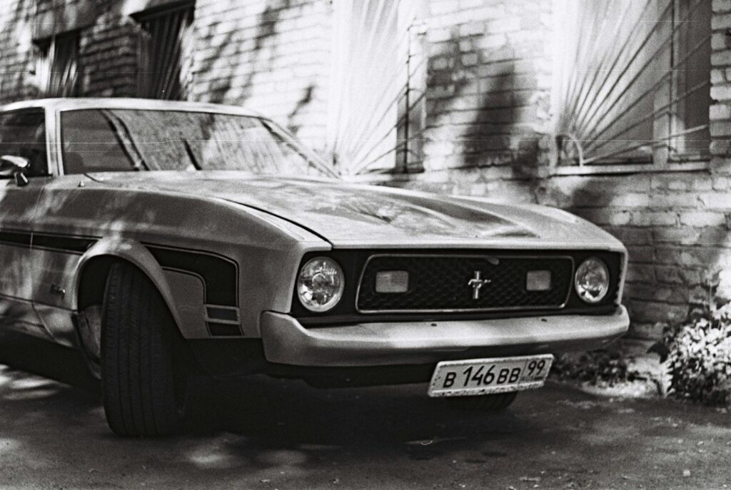 Black and white photo of a vintage Mustang parked by a brick wall, showcasing its classic design.