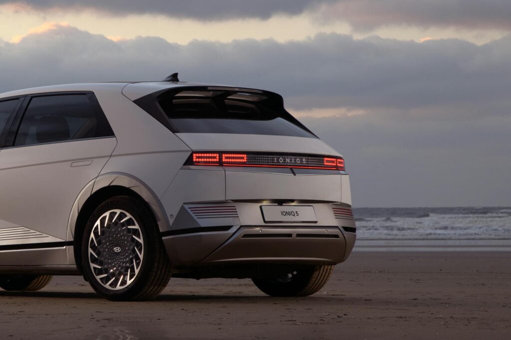 Modern electric SUV parked on a serene beach during sunset.