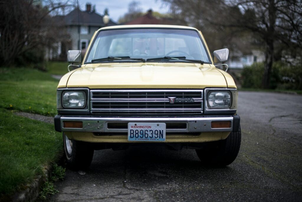 A classic yellow Toyota pickup truck parked on a quiet suburban street with Washington license plates.