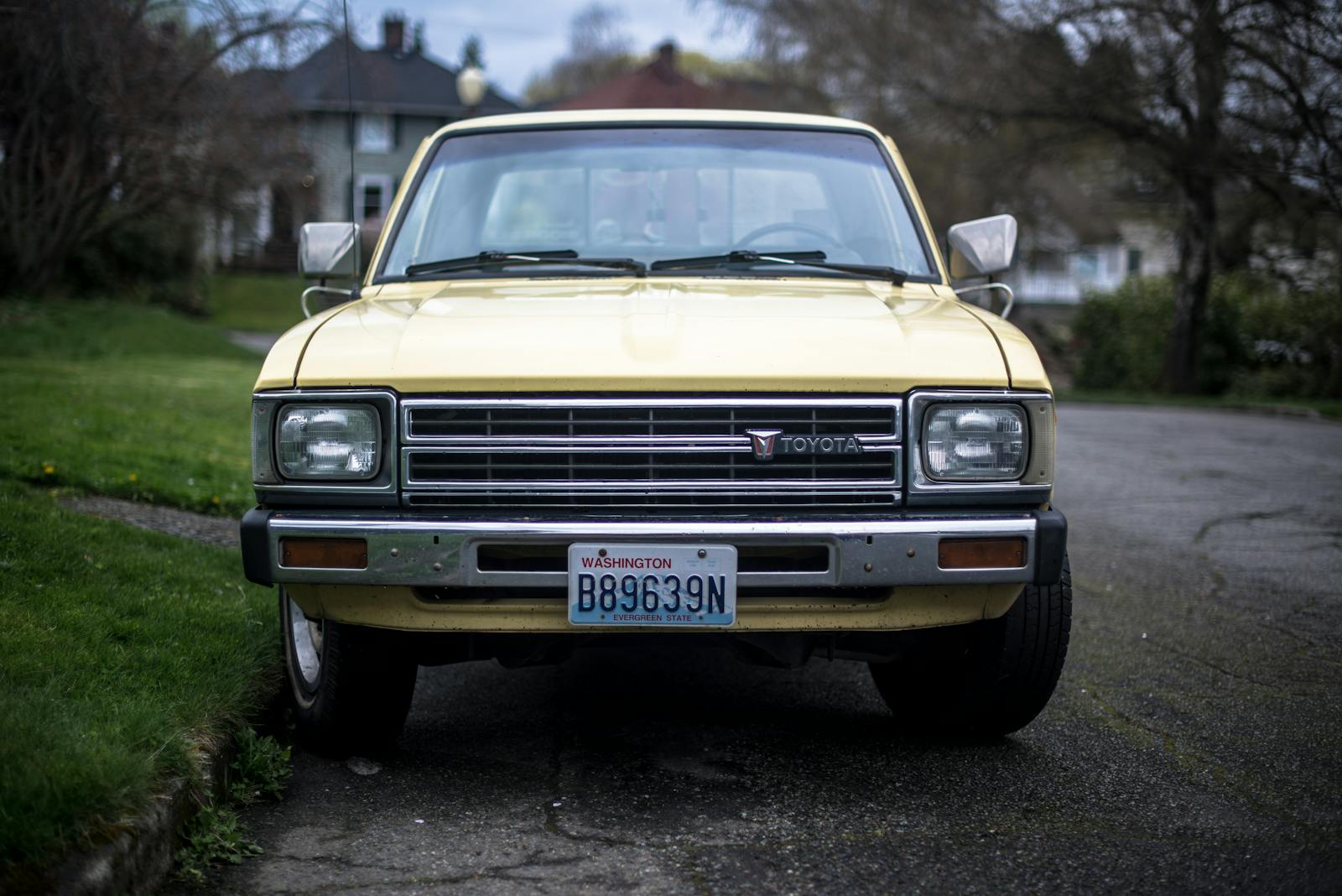 A classic yellow Toyota pickup truck parked on a quiet suburban street with Washington license plates.