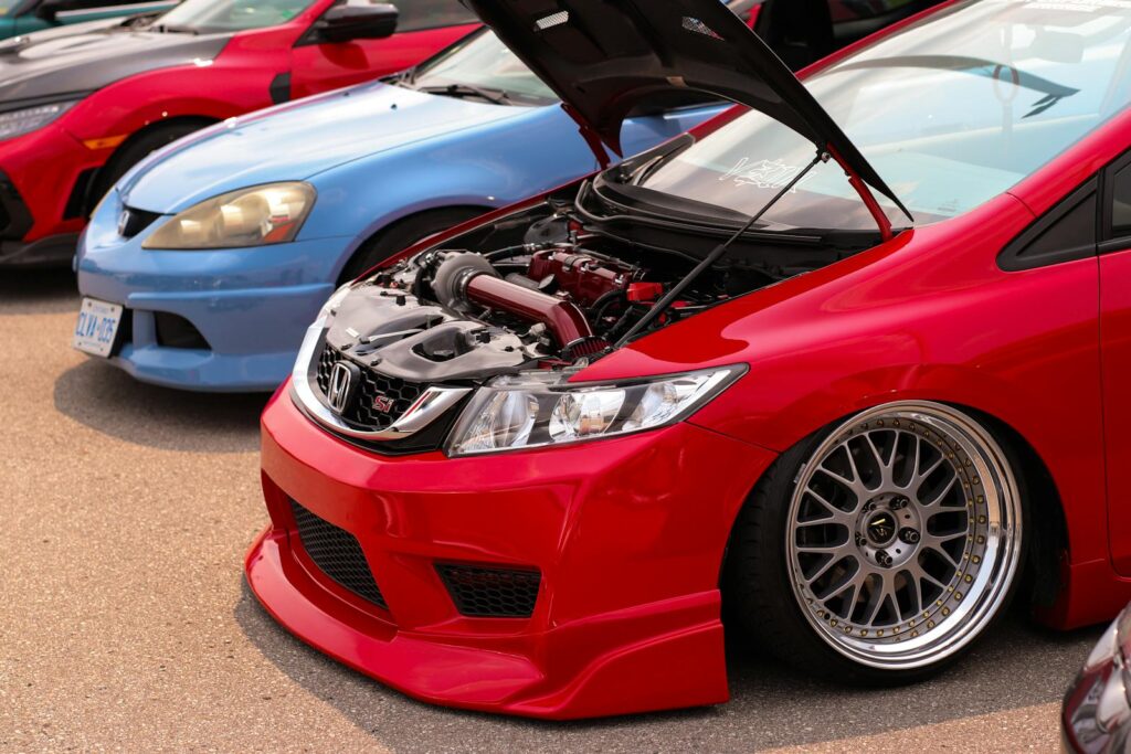 Red and blue Honda cars with hoods open, showcasing custom engines in a parking lot.